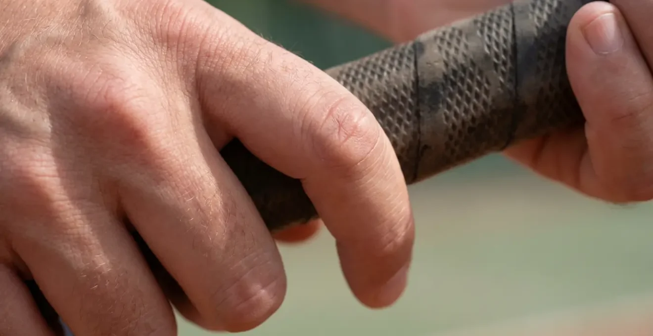 Macro shot of tennis player's hand on racket grip showing relaxed finger positioning for drop shot