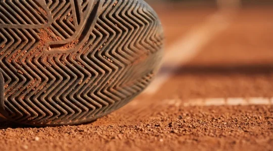 Close-up view of tennis shoe outsole with herringbone pattern on clay court surface